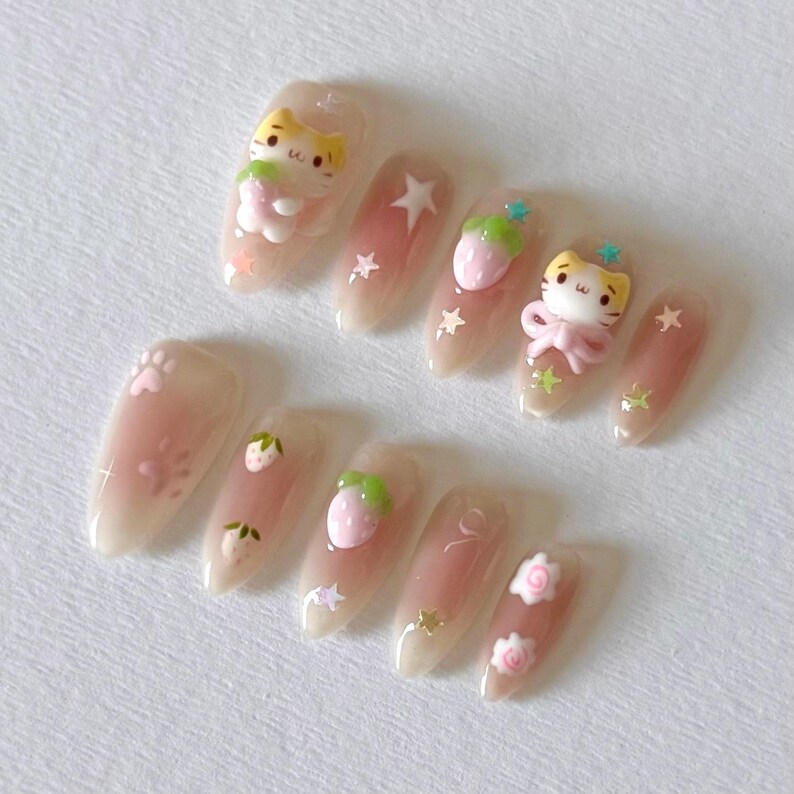 May include: Set of ten nude-colored false nails with various 3D decorations, including strawberries, stars, and cartoon cats.