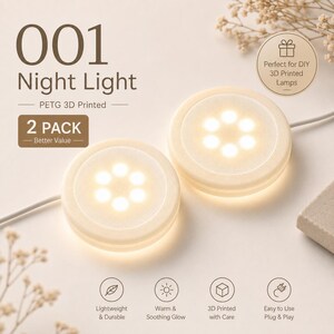 May include: A 2-pack of 001 Night Lights, which are PETG 3D printed circular devices. Each light features a warm, glowing center with six small circular LED points arranged in a hexagonal pattern. The units are white, round, and include power cords.