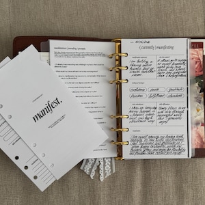 Peut inclure: Un classeur à anneaux en cuir marron contenant des feuilles blanches avec du texte noir. Les pages présentent des sections intitulées manifest, manifestation journaling prompts et currently manifesting, avec des notes manuscrites et des anneaux dorés.