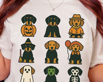 Op de afbeelding: Crèmekleurig T-shirt met een raster van cartoon teckel honden in Halloween kostuums. De honden dragen verschillende outfits, waaronder een pompoen, heks en skelet. Het woord "NATURAL" staat linksboven gedrukt.