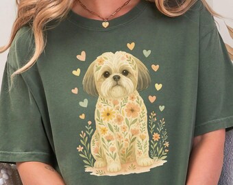 May include: A green t-shirt featuring a floral print of a Shih Tzu dog. The dog is surrounded by small hearts and flowers. The shirt has the word "HEMP" printed in the top left corner.