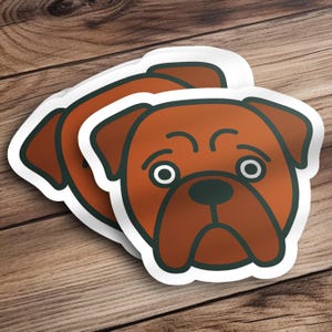 May include: A stack of stickers featuring a cartoon dog face with a brown coat, dark green outline, and white background. The dog has large, round eyes and a slightly sad expression. The stickers are on a wooden surface.