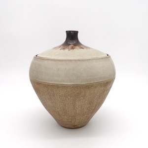 May include: A ceramic lidded jar with a textured, cone-shaped base. The jar features a light beige upper section and a darker brown, textured lower section. The lid is light beige with a dark brown top. The jar is likely used for storage.