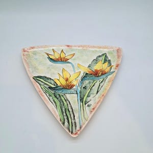 May include: A triangular ceramic dish with a hand-painted floral design. The dish features yellow flowers with green leaves and stems against a light green background. The edges are a light pink color.