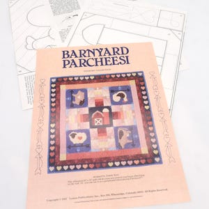 May include: A peach-colored paper with the title "BARNYARD PARCHEESI" and a quilt design featuring farm animals. The design includes a sheep, cow, and rooster. Several pattern sheets are visible in the background.