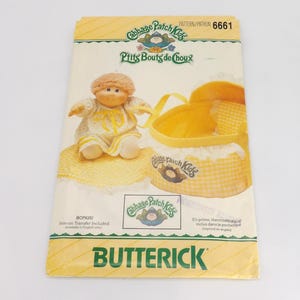 May include: A vintage Butterick sewing pattern featuring a Cabbage Patch Kids design. The pattern includes a doll, a yellow basket, and the text "Ptits Bouts de Choux". The cover is yellow and white with the text "BONUS! Iron-on Transfer Included."