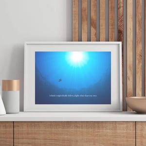 May include: A framed print with a blue and white image of a sun shining through the water. The text "I think I might finally follow a light other than my own" is printed at the bottom of the image.