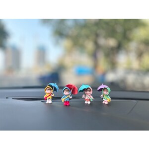 May include: Four small figurines of people holding umbrellas. The figurines are made of plastic and are painted in various colors, including blue, red, pink, and green. The umbrellas are also painted in various colors, including blue, red, pink, and green.