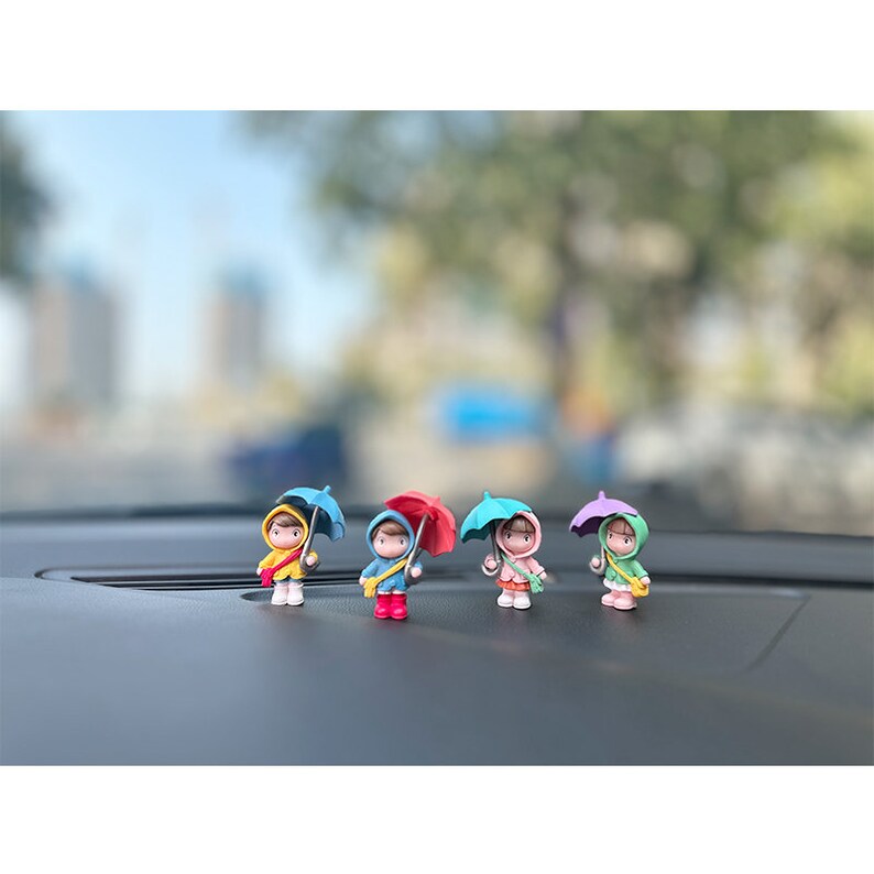 May include: Four small figurines of people holding umbrellas. The figurines are made of plastic and are painted in various colors, including blue, red, pink, and green. The umbrellas are also painted in various colors, including blue, red, pink, and green.