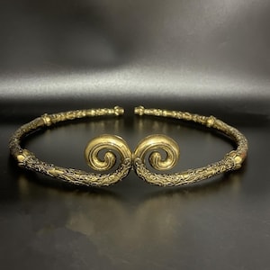 Könnte beinhalten: Eine goldfarbene Metallkrone mit aufwendigen Schnörkeln und einem Doppel-Schleifendesign.