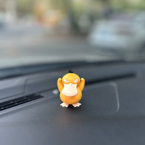 May include: A yellow duck-like figure with black eyes and a black beak, standing on a black surface. The figure has its arms raised and appears to be angry.