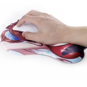 May include: A white computer mouse rests on a custom mousepad with a printed anime-style illustration. The mousepad features a padded wrist rest and a design with red, blue, and skin-tone colors.