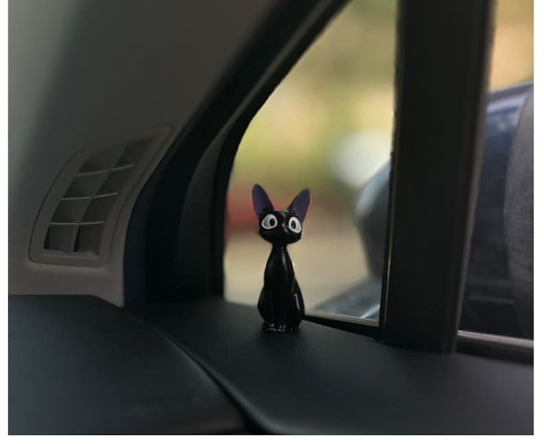 May include: Black cat figurine with large eyes, sitting on a car dashboard.