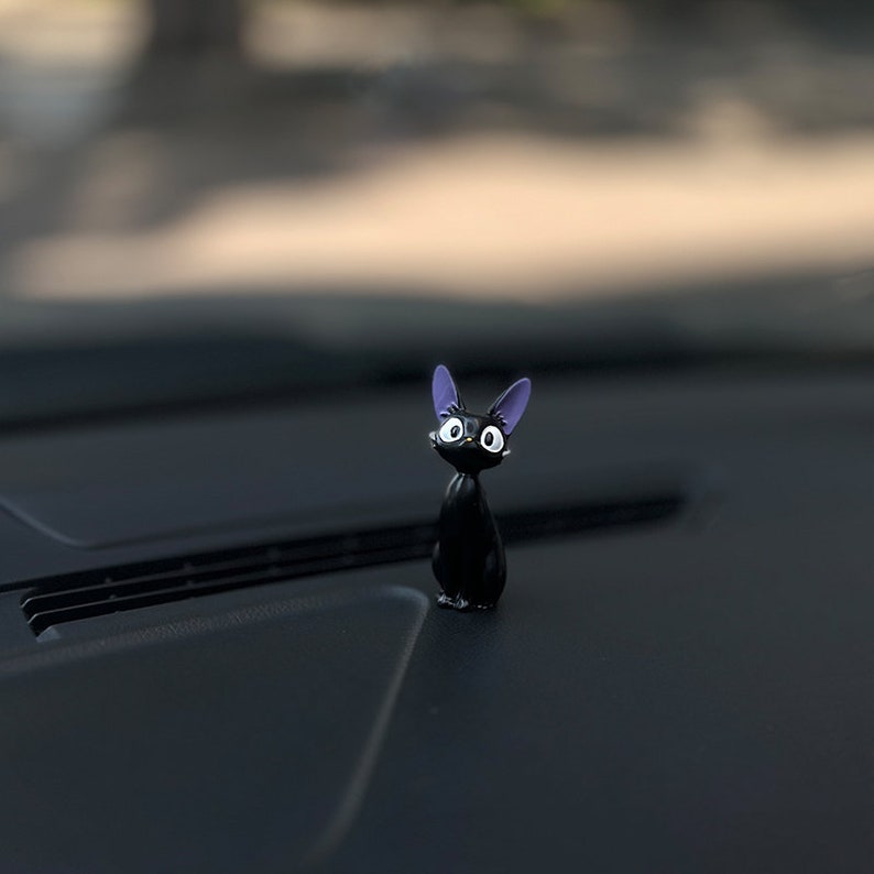 May include: A black cat figurine with purple ears and white eyes. The figurine is sitting on a black surface.
