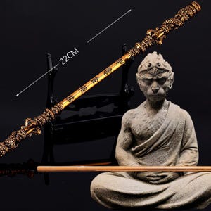 K&ouml;nnte beinhalten: Ein goldfarbener Stab mit chinesischen Schriftzeichen und einer Affenfigur, die in meditativer Pose sitzt. Der Stab ist 56 cm lang.