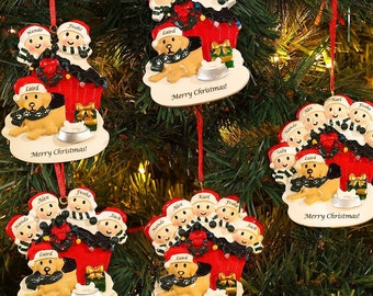 May include: Christmas tree ornaments featuring a family of people and a dog. Each ornament has a red ribbon for hanging. The ornaments are white, red, and black, with the words "Merry Christmas!" on the base.
