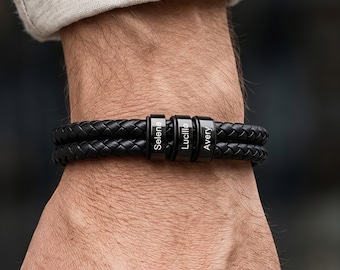 May include: A double-strand black braided leather bracelet featuring three cylindrical black metal beads. Each bead is engraved with a name, specifically Selena, Lucille, and Avery, arranged horizontally along the center of the wristband.