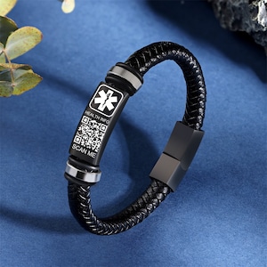 以下が含まれることがあります： ステンレス製の医療用タグが付いた黒い革のブレスレット。タグには、生命の星記号、"HEALTH INFO"と"SCAN ME"の文字、QRコードが刻まれています。