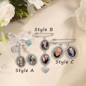 May include: Three memorial brooch styles featuring oval photo frames with ornate silver-tone borders. Style A has a white ribbon, pearl beads, and a heart charm. Style B features two stacked photo frames and a heart charm. Style C has two side-by-side frames.