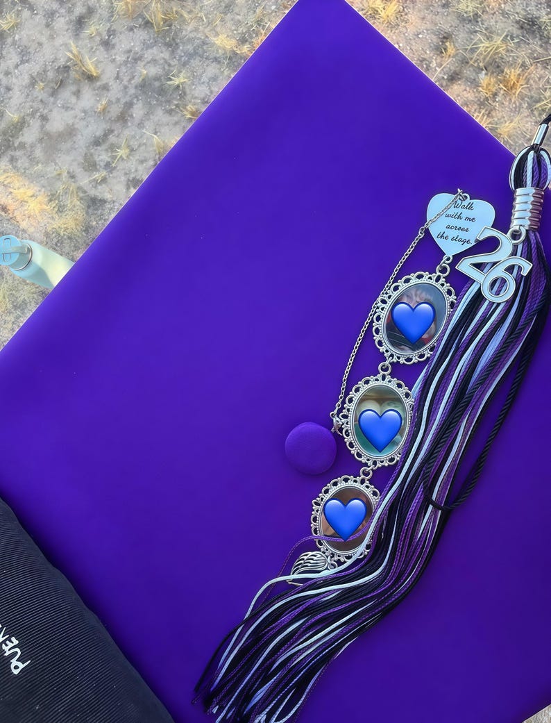 K&ouml;nnte beinhalten: Eine leuchtend violette Doktorhut-Kopfbedeckung mit einer mehrschichtigen Quaste in Violett, Schwarz und Wei&szlig;. An der Quaste befinden sich ein silberner Anh&auml;nger mit dem Text Walk with me across the stage, eine Zahl 26 und drei ovale Fotorahmen.