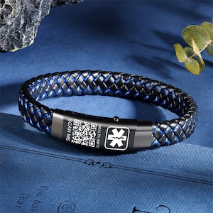 Op de afbeelding: Zwart leren armband met blauwe stiksels en een metalen plaat met een QR-code, de woorden "SCAN ME" en "HEALTH INFO", en een medisch symbool.