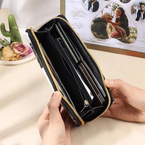 Puede incluir: Una cartera con cremallera de patr&oacute;n blanco y negro con una cremallera dorada. La cartera est&aacute; abierta y tiene m&uacute;ltiples ranuras para tarjetas y un compartimento con cremallera.
