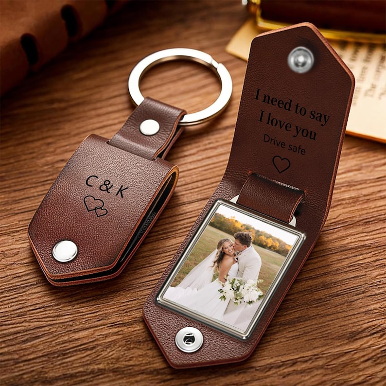 May include: A brown leather keychain with a metal ring. The closed flap features the text C&K and two hearts. The open flap reveals a photograph of a couple and the engraved text I need to say I love you Drive safe with a heart symbol.
