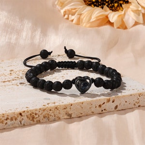 Puede incluir: Pulsera de cuentas de roca volc&aacute;nica negra con un dije de coraz&oacute;n de metal negro con un peque&ntilde;o cristal transparente. La pulsera tiene un cierre de cord&oacute;n negro.