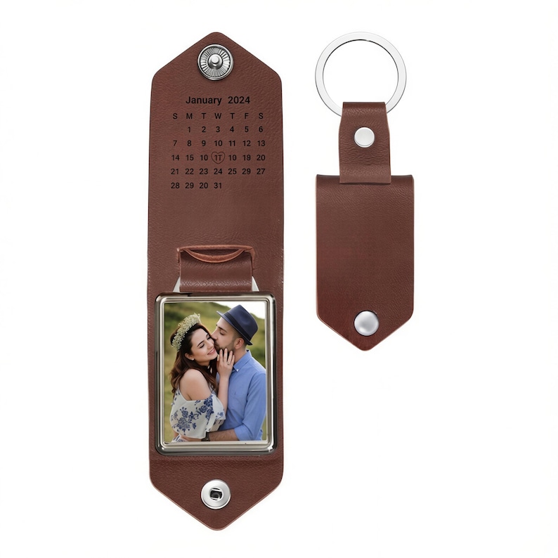 May include: A brown leather keychain featuring a fold-out design with a silver metal snap closure. The interior displays a January 2024 calendar with a heart icon on the 17th and a square frame containing a photograph of two people embracing.