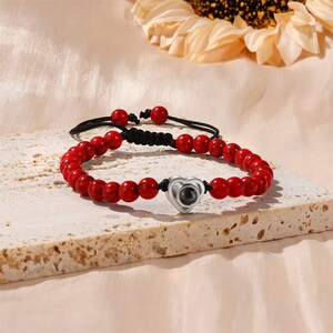 Puede incluir: Pulsera de cuentas rojas con un dije de coraz&oacute;n plateado que proyecta un mensaje cuando se ve a trav&eacute;s de un peque&ntilde;o agujero en el coraz&oacute;n.