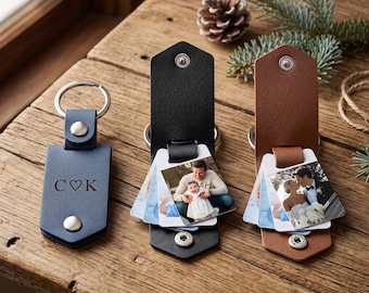 May include: Three leather-like keychains in blue, black, and brown. The blue keychain features the engraved letters C, a heart symbol, and K. The black and brown keychains each hold a small, multi-page photo album attached to a metal ring with a snap closure.