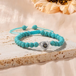 Puede incluir: Un brazalete de cuentas turquesa con un dije de coraz&oacute;n plateado que presenta una peque&ntilde;a piedra iridiscente. El brazalete tiene un cord&oacute;n azul con nudos ajustables.