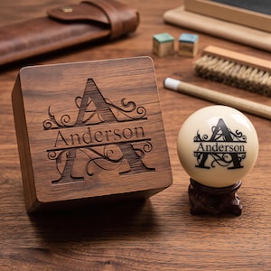 May include: A square dark wood box with a laser-engraved letter A and the name Anderson, paired with a matching cream-colored spherical object on a small dark wooden stand, both featuring the same personalized monogram design.