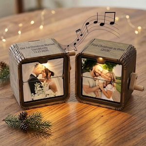 Puede incluir: Dos cajas de música de madera con manivelas, cada una con una fotografía. La caja izquierda está grabada con 'Our 1st Christmas Married Liam&Emily 12.25.2026.' La caja derecha está grabada con 'First Christmas as three (2026).'