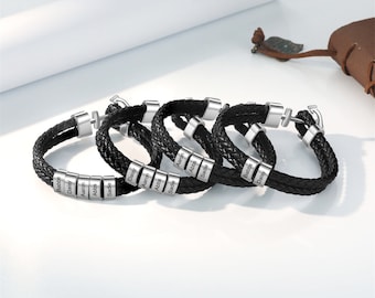 May include: Five black leather bracelets with silver metal beads. Each bead is engraved with a different name: Babbie, Daisy, Aaron, Abbie, Sadie, Aaron, Abbie, Sadie, Babbie, Daisy.