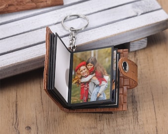 Puede incluir: Llavero de cuero marrón con un álbum de fotos y un anillo plateado. El álbum tiene varias páginas y presenta una foto de una mujer y una niña.