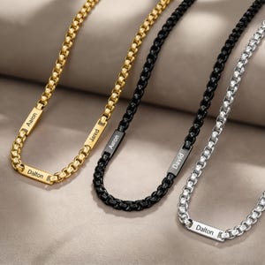 Peut inclure: Quatre colliers personnalisés en or, noir et argent. Chaque collier est composé d'une chaîne carrée et d'un pendentif rectangulaire gravé d'un nom. Les noms visibles sont Aaron, Jared, David et Dalton.
