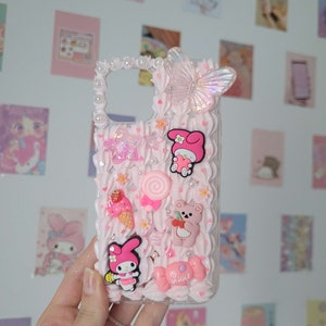 May include: A pink and white phone case with a 3D design featuring a butterfly, a bear, a lollipop, a strawberry ice cream cone, and a character from the cartoon My Melody. The case has a glittery star and the word "Love" written on it.