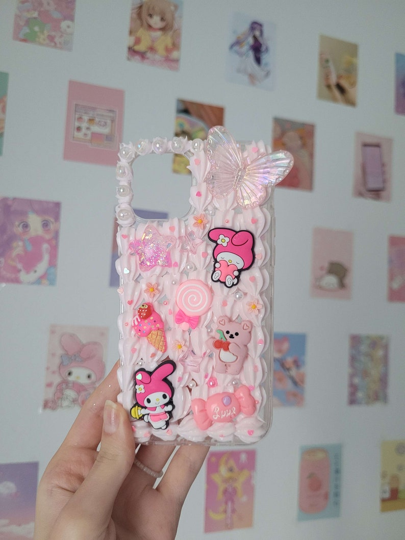 May include: A pink and white phone case with a 3D design featuring a butterfly, a bear, a lollipop, a strawberry ice cream cone, and a character from the cartoon My Melody. The case has a glittery star and the word "Love" written on it.