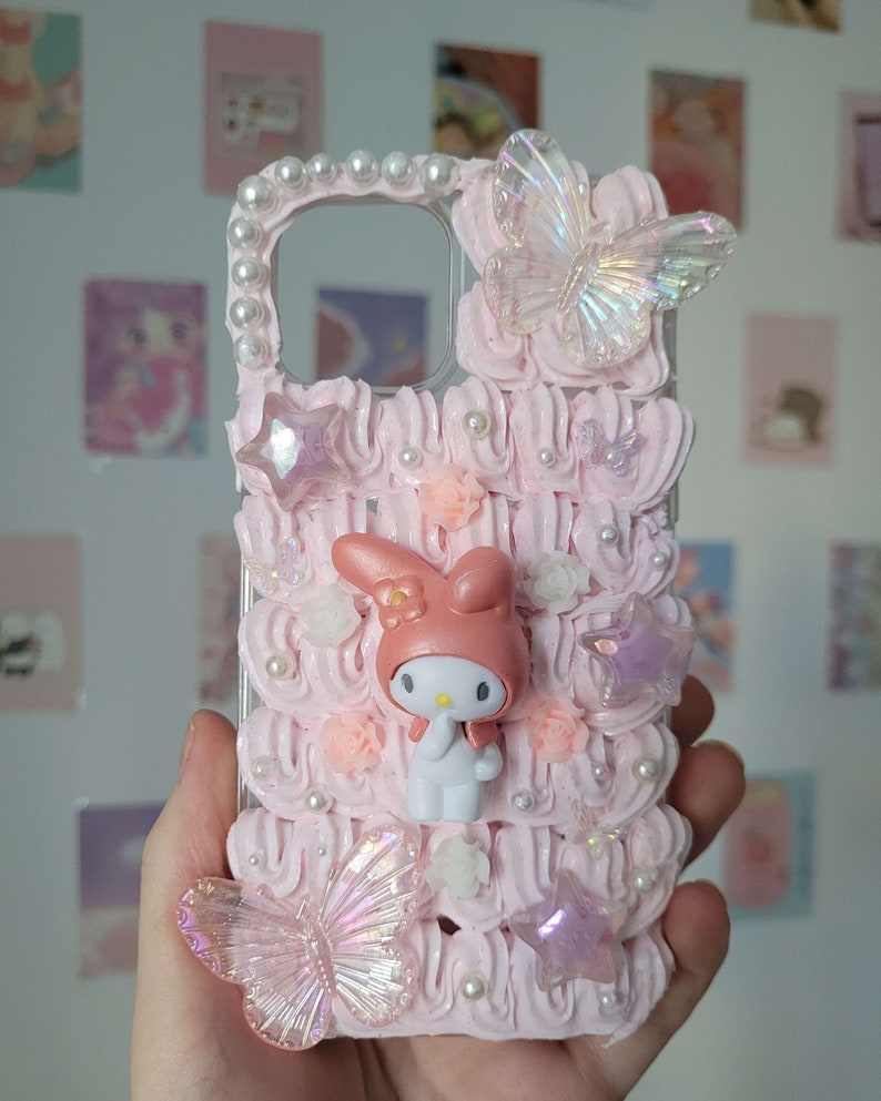 May include: A pink and white phone case with a 3D Hello Kitty character, two iridescent butterflies, and pearl accents.
