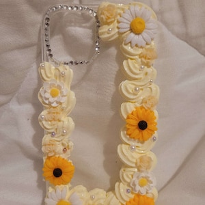 Peut inclure: Une coque de t&eacute;l&eacute;phone transparente d&eacute;cor&eacute;e de fleurs blanches et jaunes. La coque a une bordure scintillante et est orn&eacute;e de perles blanches.