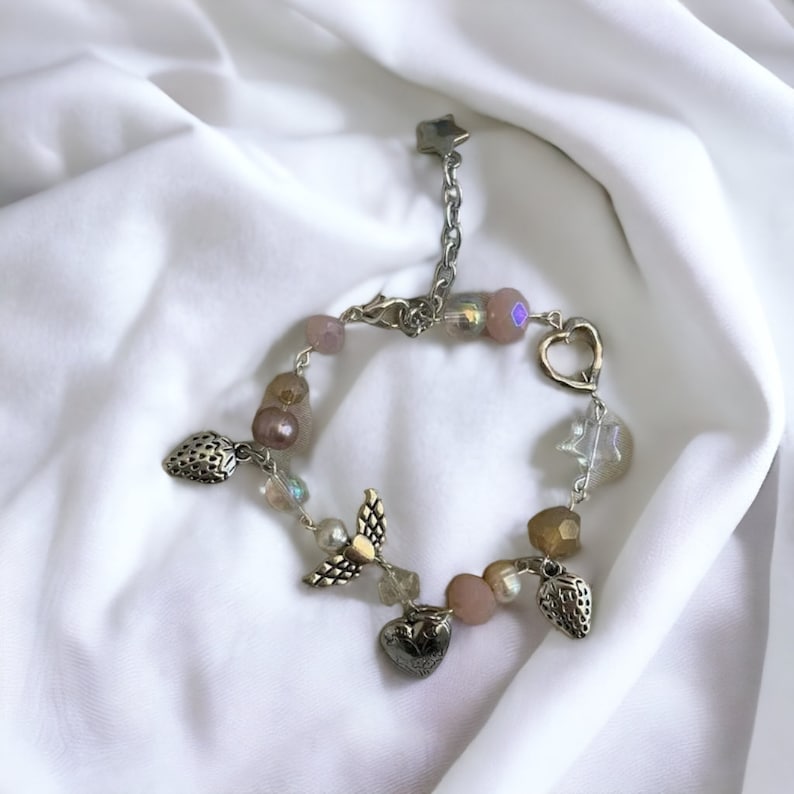 Op de afbeelding: Een zilveren armband met roze en heldere kralen, met aardbei- en hartcharms. De armband heeft een stervormige sluiting.