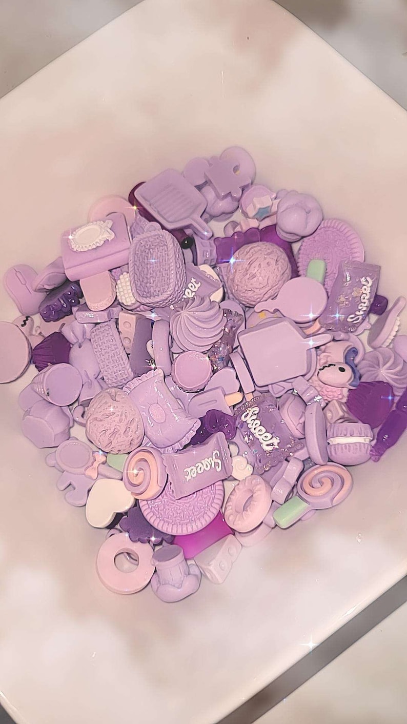 Puede incluir: Una colecci&oacute;n de abalorios de resina de color lavanda con formas variadas, como helados, galletas y caramelos. Algunos abalorios tienen la palabra "Sweet". Los abalorios est&aacute;n en un cuenco blanco.