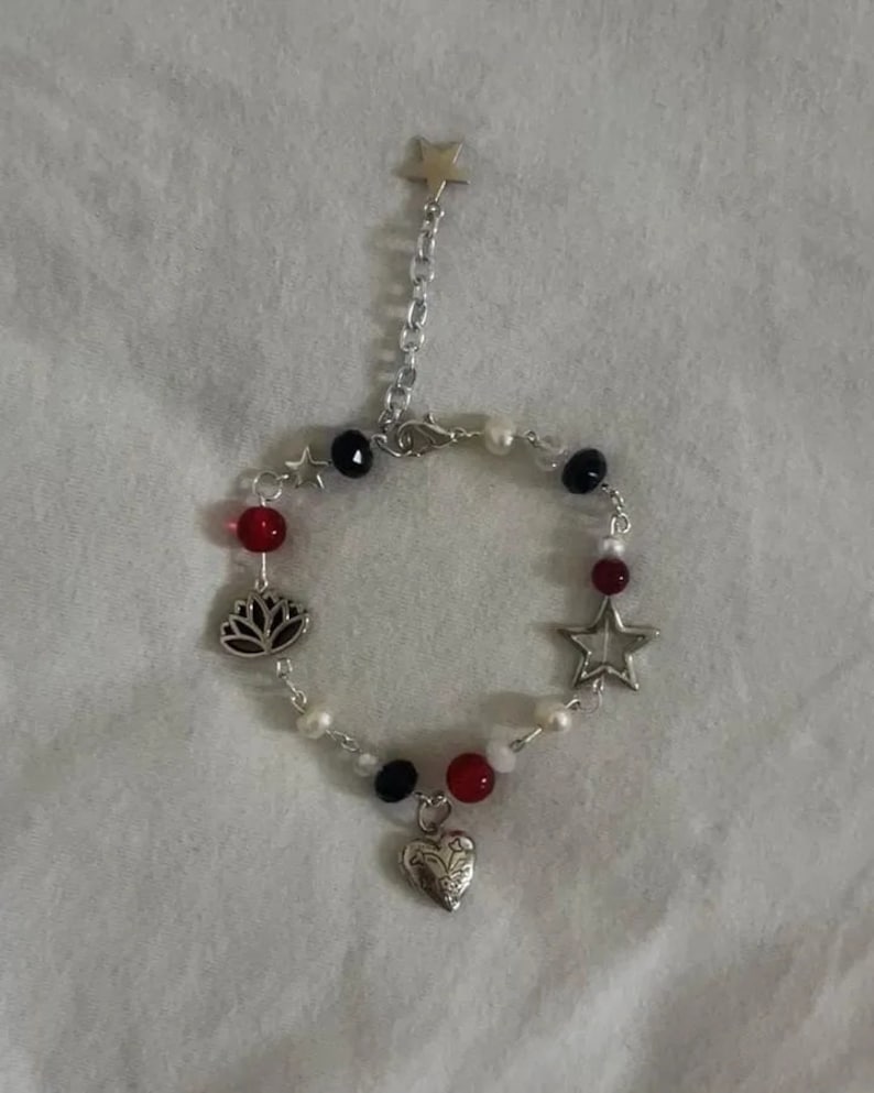 Op de afbeelding: Een zilveren armband met rode, witte en zwarte kralen. De bedels zijn een ster, een hart en een lotusbloem.