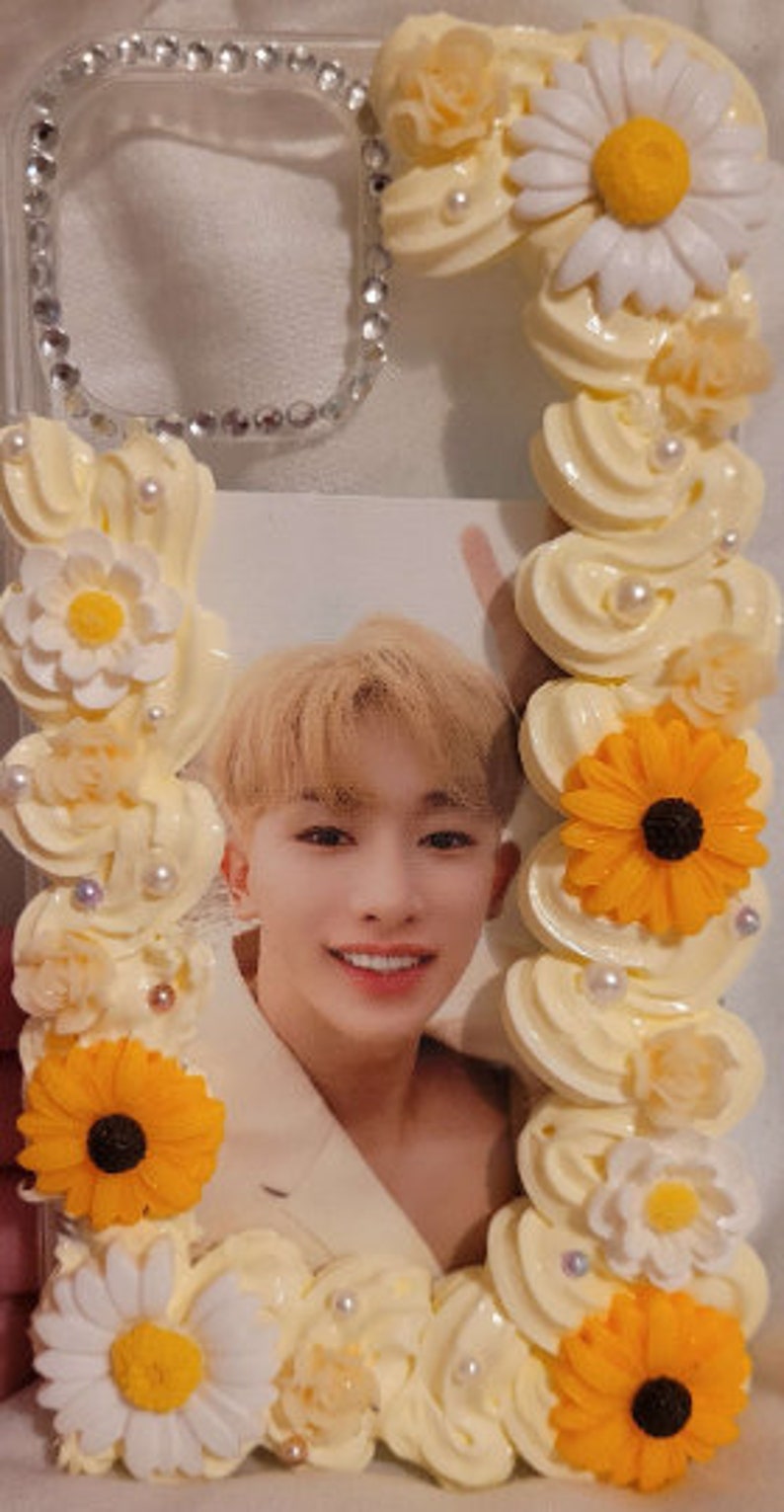 Peut inclure: Une coque de t&eacute;l&eacute;phone transparente d&eacute;cor&eacute;e de fleurs blanches et jaunes, d'un motif en spirale blanc et jaune, et d'une photo d'un jeune homme.
