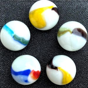 May include: Five white marbles with colourful swirls of yellow, blue, green, red, and brown. Each marble has a unique pattern, creating a vibrant and playful assortment. The marbles are arranged on a dark textured surface.