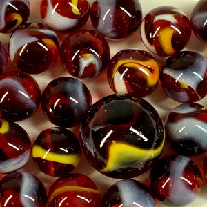 Puede incluir: Una colección de canicas de vidrio de varios tamaños. Las canicas presentan patrones arremolinados de rojo, blanco, amarillo y negro. Las superficies brillantes reflejan la luz, creando una exhibición vibrante y llamativa.