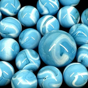 Puede incluir: Una colección de canicas de vidrio azul y blanco con remolinos. Las canicas varían en tamaño, con una canica grande en el centro. Las canicas tienen un acabado brillante y están dispuestas sobre un fondo oscuro.