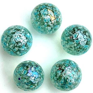 May include: Five glass marbles with a speckled, textured appearance. The marbles are primarily teal and turquoise, with iridescent accents. The spheres are arranged against a white background, showcasing their unique, decorative design.
