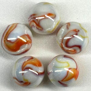 Może przedstawiać: Pięć zabytkowych kulek szklanych. Każda kulka ma białą podstawę z wirującymi wzorami w kolorze pomarańczowym, czerwonym i żółtym. Kulki są okrągłe i mają błyszczące wykończenie, prezentujące kolorowe wzory.